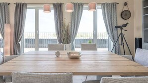 A dining area with a wooden table, grey upholstered chairs, a vase with dried plants, and a telescope on a tripod. - SeeZeichen Nordstrand by Interhome (Nordstrand)