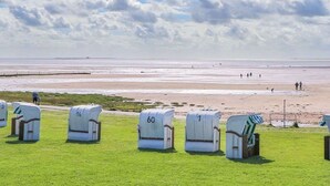 A beach with white wicker chairs numbered 1, 60, and 16, and a large sculpture. - SeeZeichen Nordstrand by Interhome (Nordstrand)