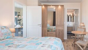 A bedroom with a bed, a desk, a chair, a mirror, and a bathroom visible through an open door. - SeeZeichen Nordstrand by Interhome (Nordstrand)