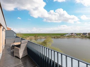 Un balcon doté de meubles en osier, donnant sur un lac, avec une vue sur des maisons situées au loin.