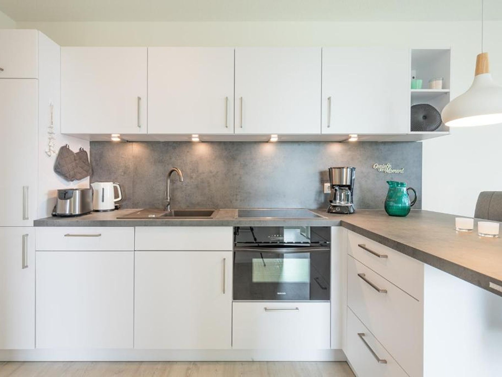A modern kitchen with white cabinets, a stainless steel sink, a coffee maker, and a built-in oven.