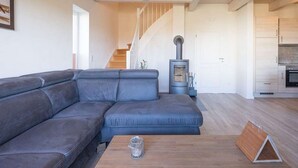 Un salon moderne avec un canapé d’angle, une table basse en bois et un poêle à bois encastré.