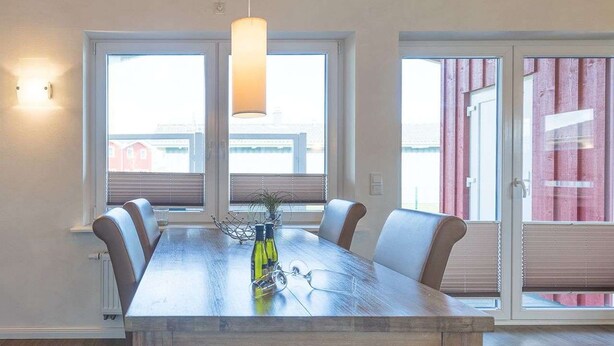 Un espace repas comprenant une longue table en bois, six chaises et un luminaire suspendu.