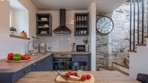 A modern kitchen with a stone wall, a clock, and a wooden table with vegetables.