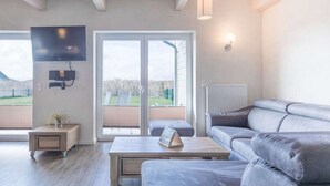 A modern living room with a grey sofa, a coffee table, a TV mounted on the wall, and a sliding glass door leading to a balcony. - Basstölpel by Interhome (Dagebüll)