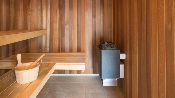 A sauna room with wooden benches, a wooden bucket, and a sauna heater.