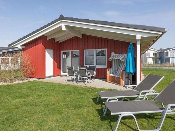 Ein rotes Gebäude mit überdachter Terrasse, Außenbestuhlung und einem blauen Sonnenschirm.