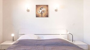 A bedroom with a bed, white headboard, two bedside tables, and a wall-mounted painting. - Vacation home Föhr by Interhome (Dagebüll)