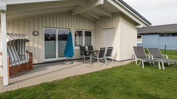 A covered patio area with a table and chairs, a striped chair, and a blue umbrella. - Vacation home Föhr by Interhome (Dagebüll)