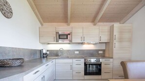 A modern kitchen with wooden cabinets, a stainless steel oven, and a microwave. - Vacation home Föhr by Interhome (Dagebüll)