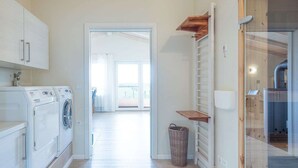 Un cuarto de lavandería con lavadora y secadora, una cesta de mimbre y un vidrio corredizo que da a un balcón.
