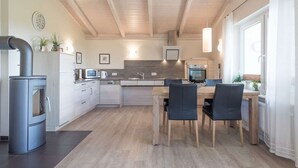Una cocina moderna con estufa integrada, un comedor con mesa y sillas, y un amplio ventanal con persianas.