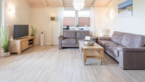 Una sala de estar moderna con un sofá, una mesa de centro, un televisor y una lámpara colgante.
