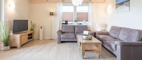 A modern living room with a sofa set, a coffee table, a TV, and a pendant light.