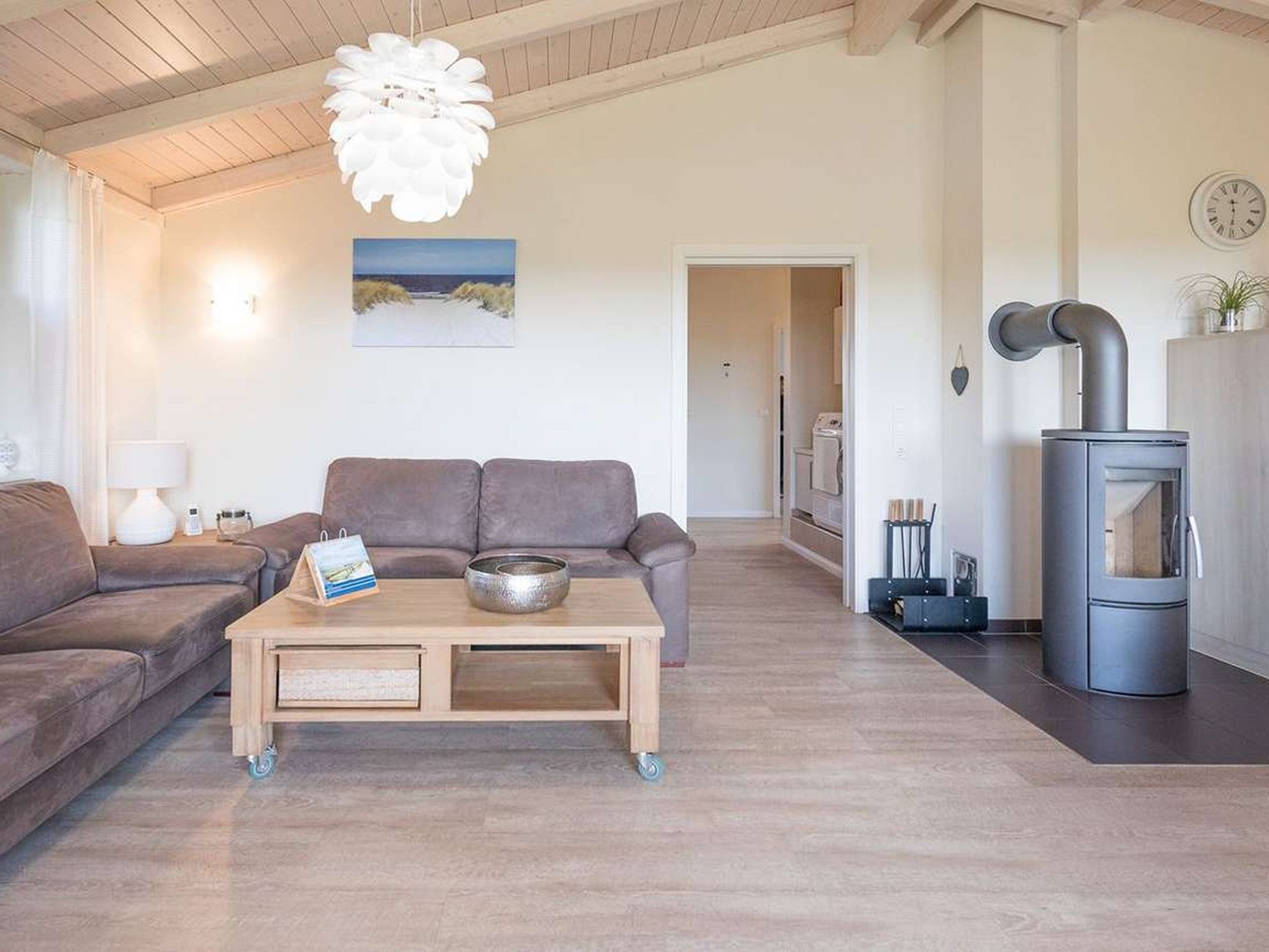 Un salon chaleureux avec un canapé, une table basse en bois, un luminaire suspendu et un coin cuisine équipé d’une cuisinière.