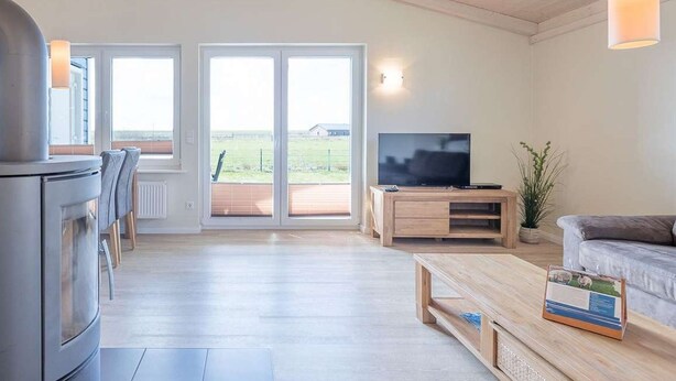 A modern living room with a TV, wooden furniture, and a large sliding glass door leading to a deck. - Syltrose by Interhome (Dagebüll)