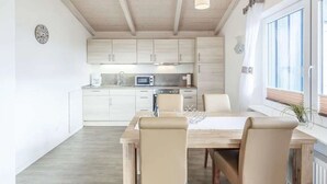A modern kitchen with white cabinets, a dining area with a wooden table and chairs, and a window with blinds. - Wattschnecke by Interhome (Dagebüll)