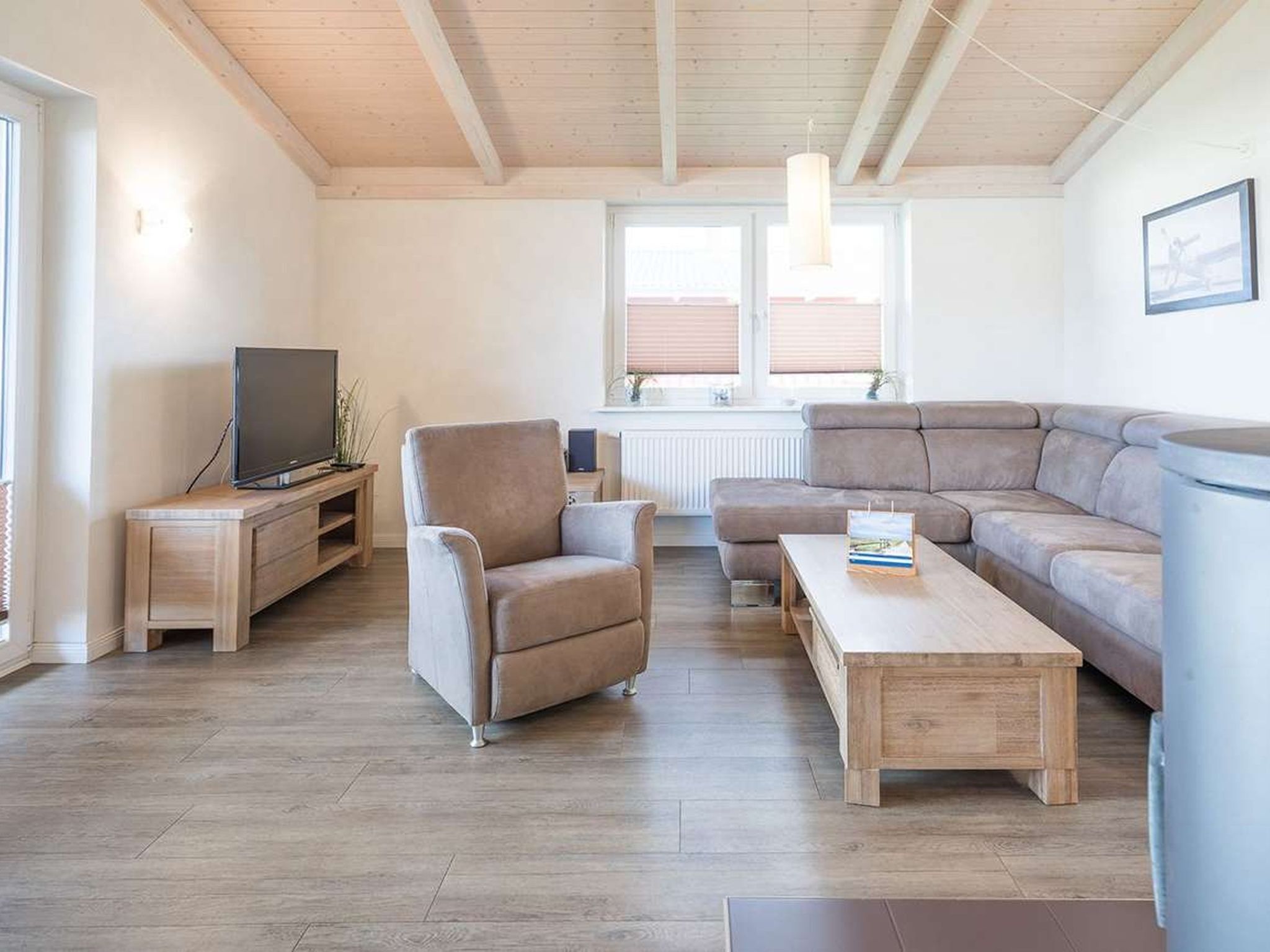 Una sala de estar moderna con piso de madera, un sofá gris, una mesa de centro de madera, un sillón gris y un televisor sobre un mueble de madera.