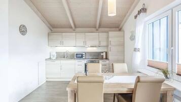 Eine moderne Küche mit weißen Schränken, ein Essbereich mit Holztisch und -stühlen sowie ein Fenster mit Jalousien.