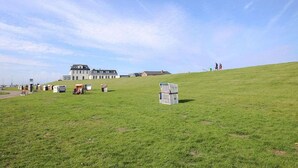 Un campo cubierto de hierba con un edificio grande al fondo, algunas construcciones en la colina y un cielo despejado.
