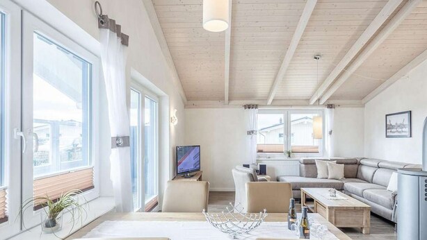 Una sala de estar moderna con techo de madera, un comedor con mesa y sillas, un sofá y un televisor.