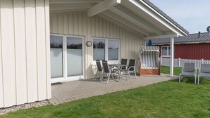 A covered patio area with a table and chairs, a small covered seating area, and a white picket fence. - Steinwälzer by Interhome (Dagebüll)