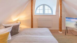 Ein Schlafzimmer mit Schrägen, einem Oberlicht, einem Bett mit Kissen, einem Heizkörper und einem Fernseher auf einem Schrank.