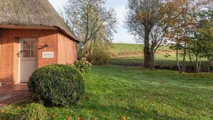 Ein Backsteinhaus mit einem Reetdach, einem gepflegten Rasen und Bäumen im Hintergrund.