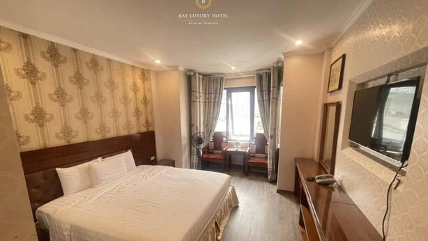 Une chambre d’hôtel avec un grand lit, un bureau, une chaise, une télévision et une fenêtre avec des rideaux.