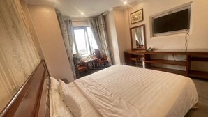 Une chambre d’hôtel avec un grand lit, un bureau avec une chaise, une t élévision et une fenêtre avec des rideaux.