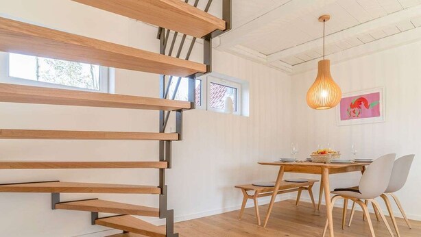 A modern interior with a wooden staircase, a dining area with a table and chairs, and a pendant light.