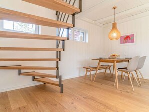 Un intérieur moderne avec un escalier en bois, un coin repas comprenant une table et des chaises, et un luminaire suspendu.