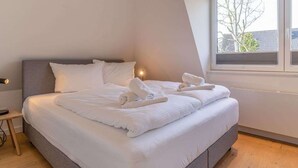 A modern hotel room with a large bed, a bedside table, and a window with a view of the outside.