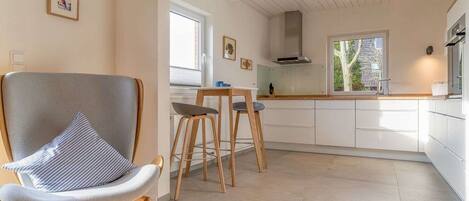 A modern kitchen with white cabinets, a wooden dining table, and two bar stools.
