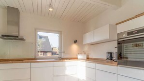 A modern kitchen with white cabinets, a wooden countertop, a built-in oven, and a window providing a view of the outside.