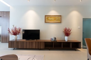 Una sala de estar moderna con un televisor de pantalla plana sobre un mueble de madera, dos jarrones con flores rojas y una obra de arte enmarcada en la pared.