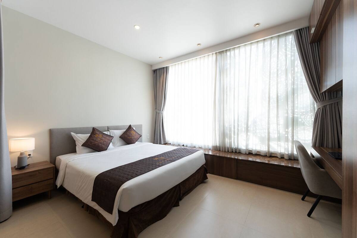 Ein Hotelzimmer mit einem großen Bett, einem Schreibtisch und einem Fenster mit Vorhängen.