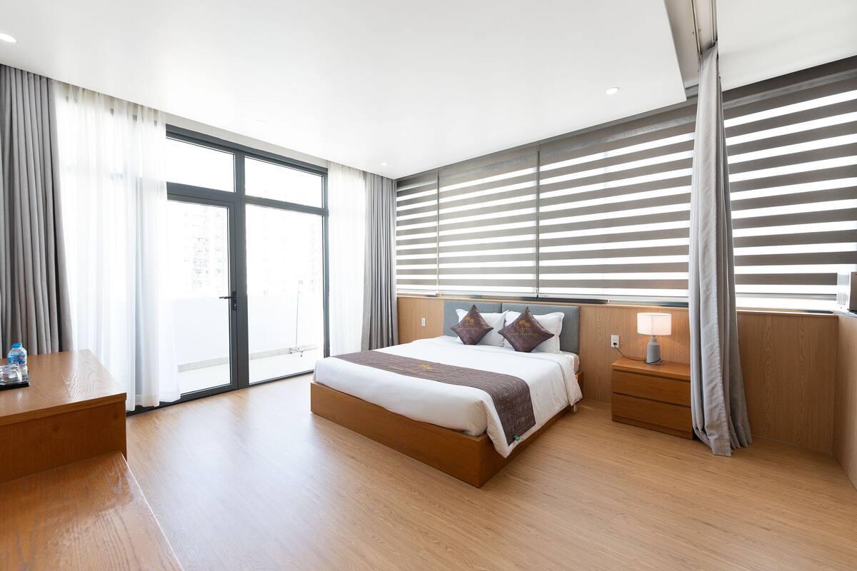 Ein modernes Hotelzimmer mit einem großen Bett, Holzboden, einem Schreibtisch und Blick durch das Fenster.