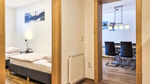 A hotel room with a bed, bedside table, lamp, and a view of another room with a dining table and chairs. - Apart Dawin by Interhome (Strengen)
