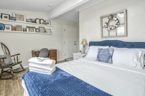 Quarto com uma cama, uma cadeira de balanço, cômoda e uma parede com quadros.