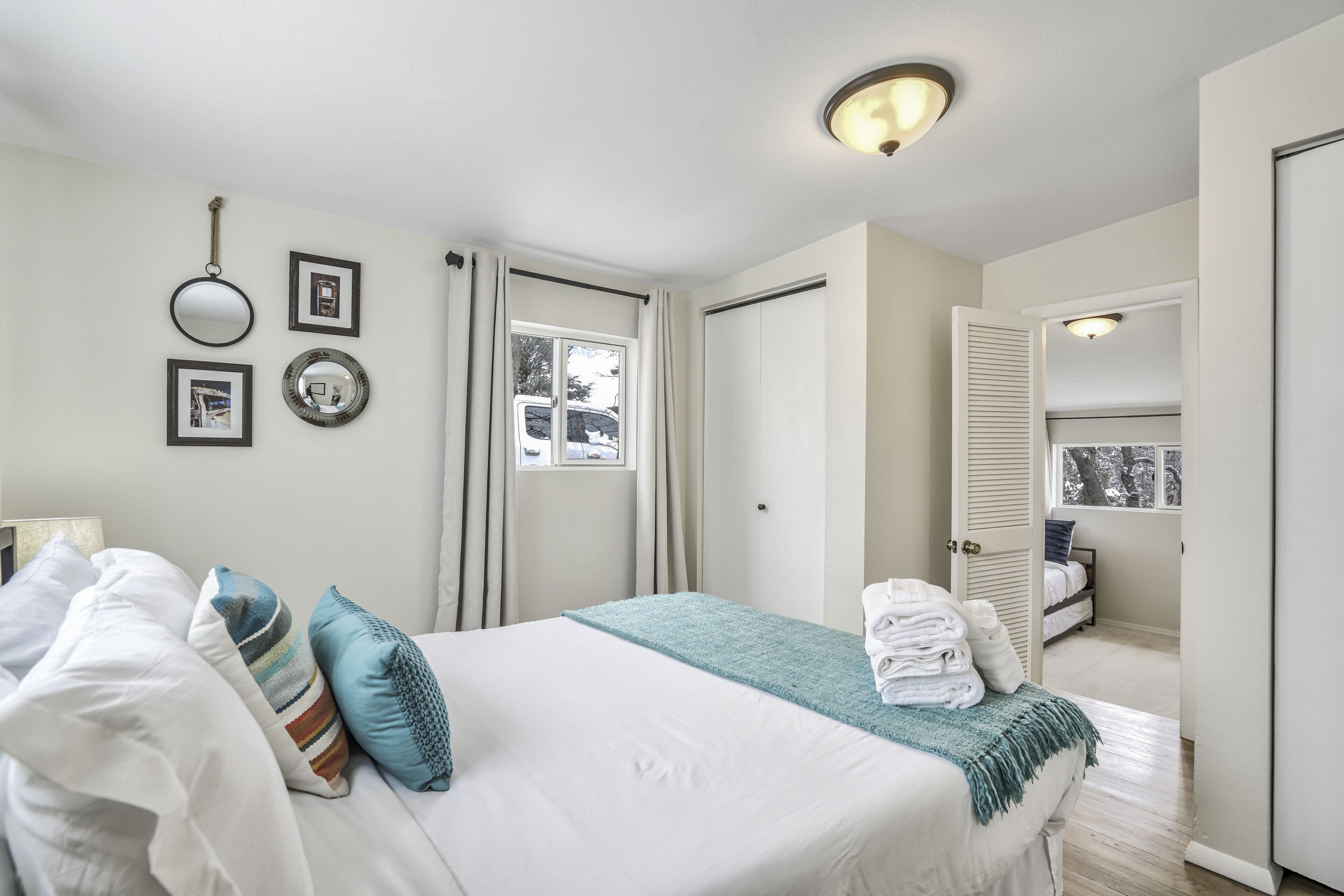 Une chambre à coucher bien rangée, avec un lit, des oreillers, une table de chevet, un miroir et une fenêtre avec des rideaux.