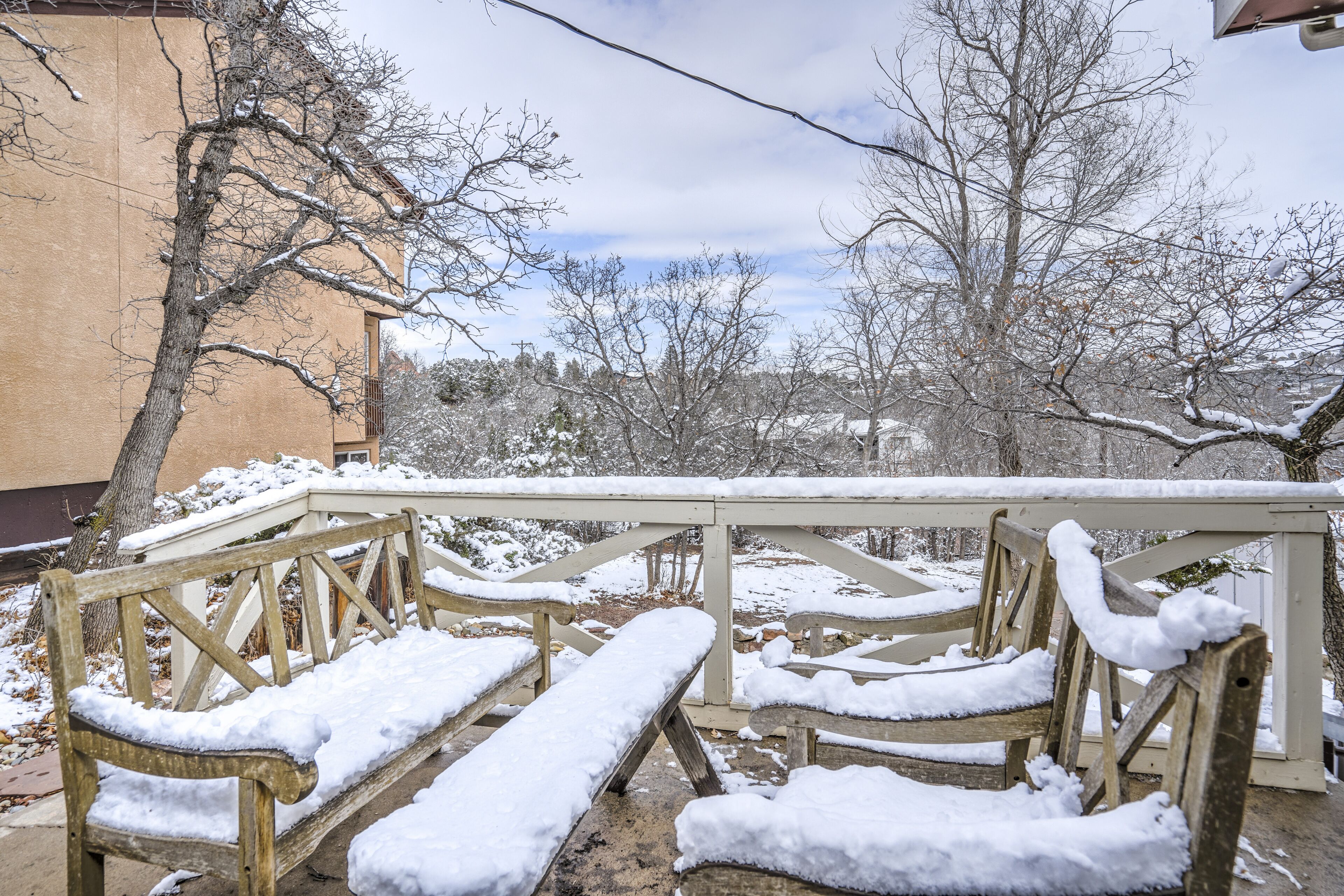A wooden bench with snow on it, a railing, and a tree in the background.
