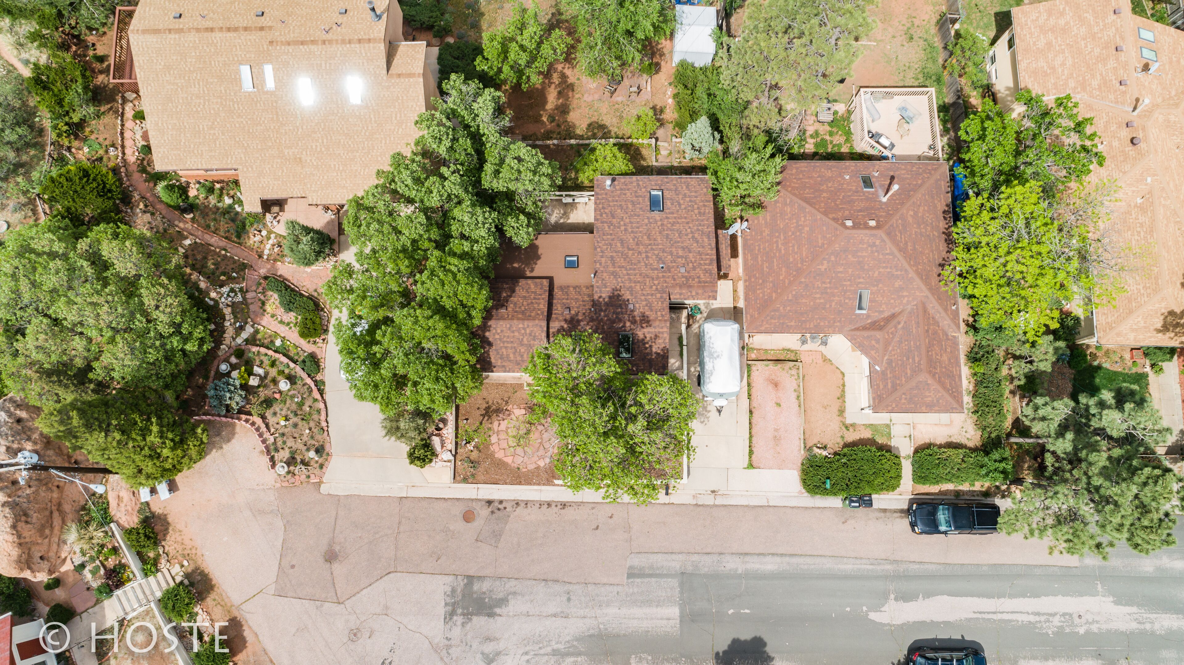 An aerial view of a residential area with multiple houses, a paved driveway, and surrounding greenery.