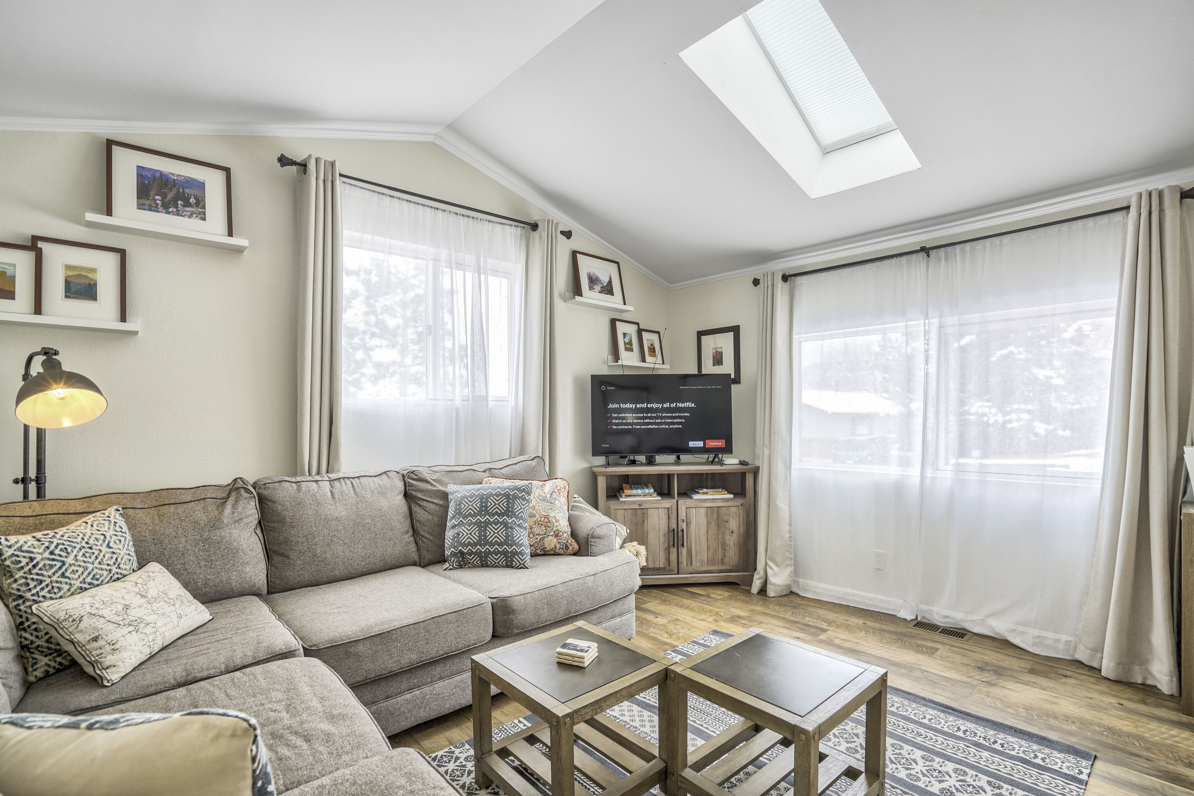 A living room with a sectional sofa, a flat-screen TV, wooden flooring, and a skylight.