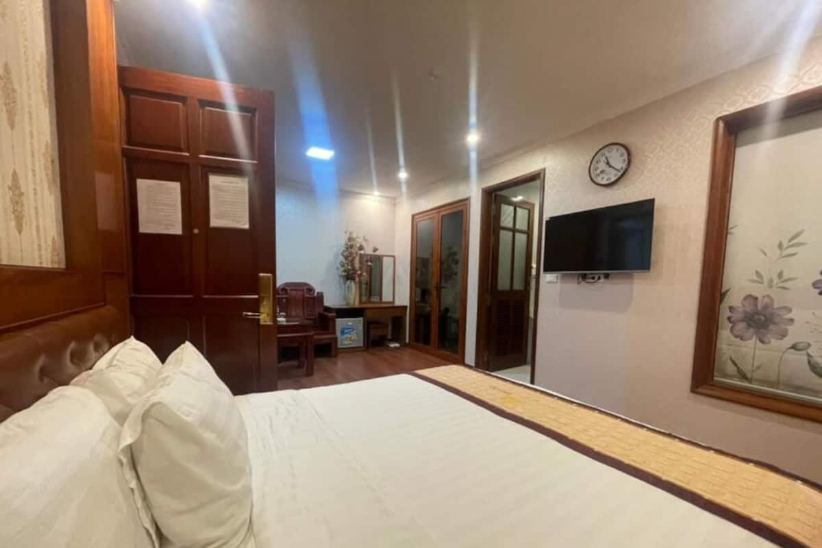 A hotel room with a bed, a television, a clock, and a door.