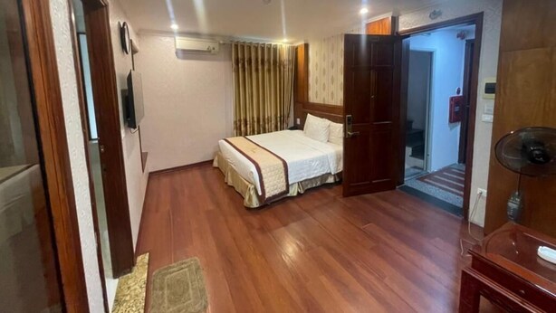 A hotel room with a wooden floor, a bed with a white bedspread, a wooden wardrobe, and a desk with a lamp. - Ngoc Lan 2 Hotel- by Bay Luxury (Hanoi)