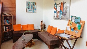 A cozy living room with a brown sofa, orange cushions, a wooden coffee table, a bookshelf, and a painting of sailboats. - SamaraChilloutLodge (Sámara)