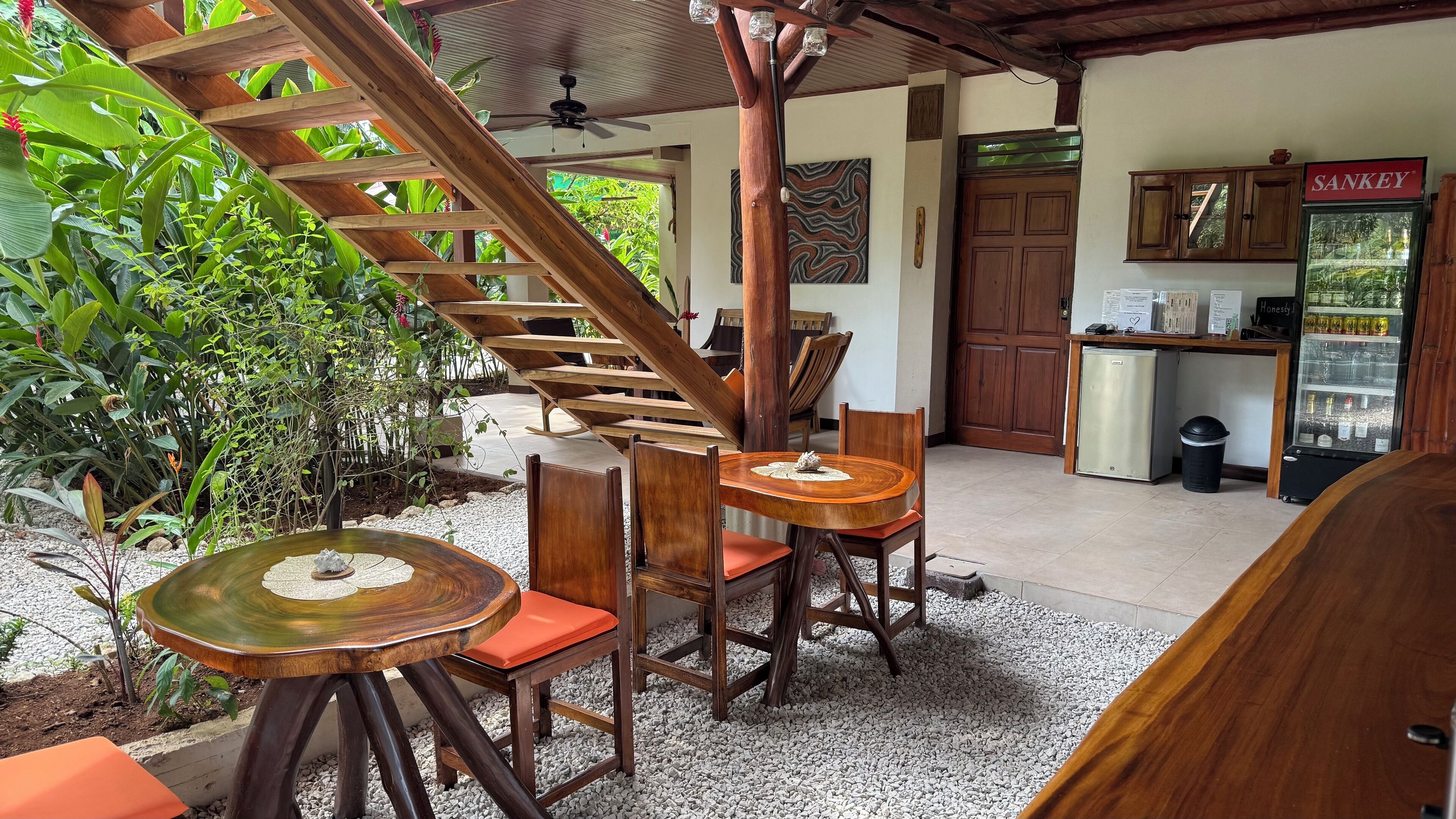 A wooden staircase leading to a covered area with a table and chairs, a refrigerator, and a door labeled "SANKEY".