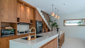 Eine moderne Küche mit Holzausstattung, einer großen Kochinsel mit Spüle und Pendelleuchten.