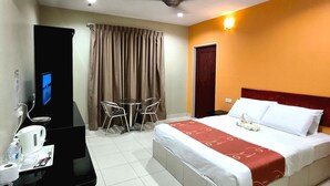 Een hotelkamer met een bed, een bureau met een computer, een stoel, een tafel en een plafondventilator.